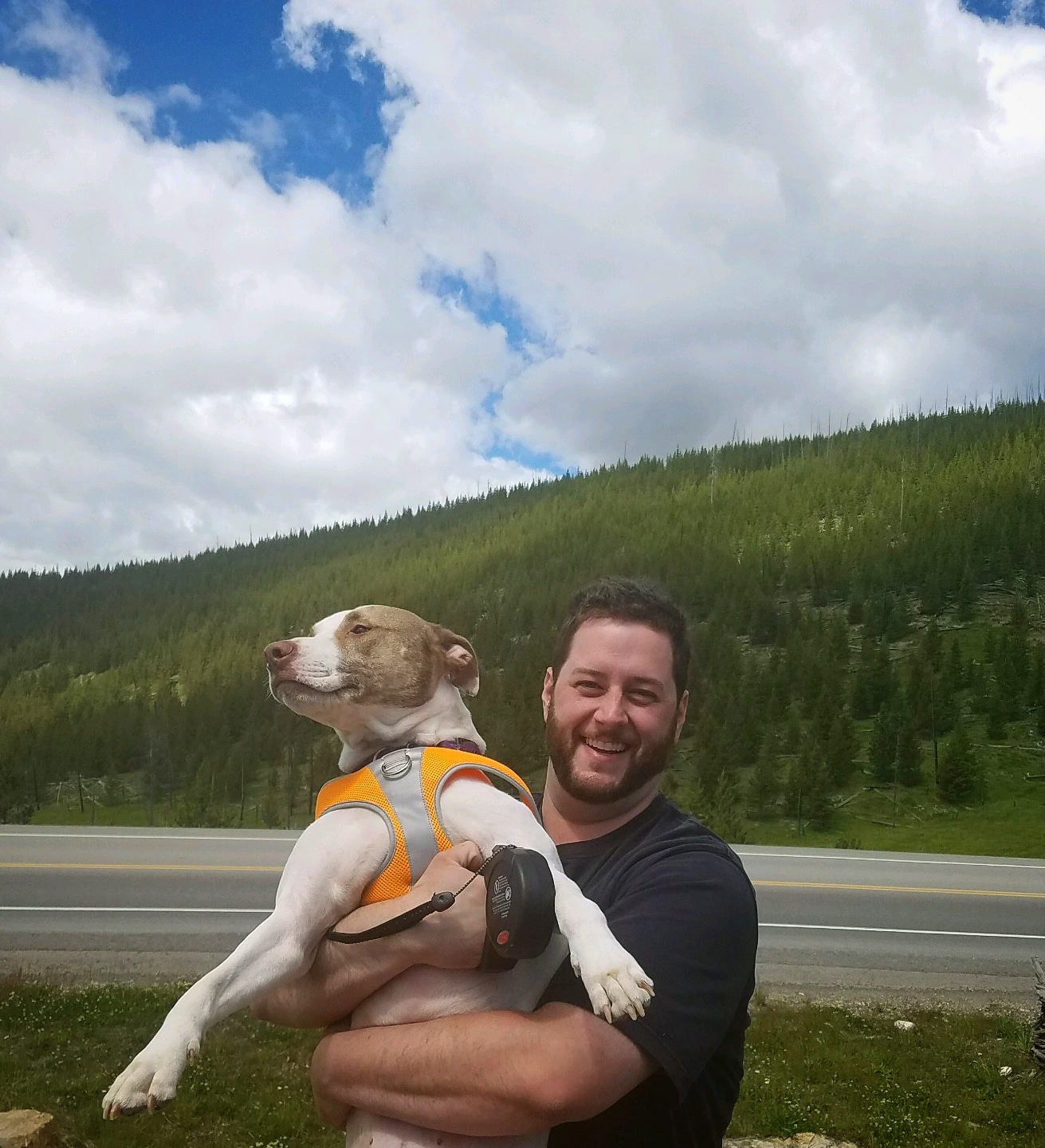 Fired Home Depot Union organizer Steve Pace holds a dog in front of a road and a green wooded hill